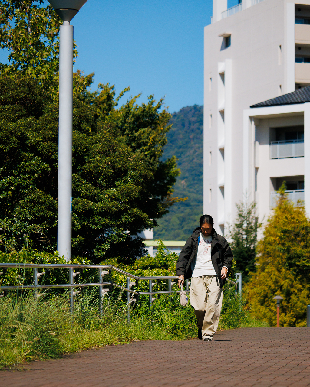 乾いた光と、神戸の広い空。


広い歩道と乾いた舗装
伸びた草の向こうには山が見える。

そんな景色の中を
Dark OliveのジャケットとKhakiのパンツで歩く。

少し土っぽい色の組み合わせが
赤茶の道や緑の残る景色と自然につながっていく。

強い日差しが入ると暗いジャケットにもやわらかな表情が生まれ
パンツには歩くたびに影が残る。

海の近くにいながらふと振り返ると山がある。
神戸らしいこの距離感を感じた日のスタイル。


Model：173㎝　
Nakamura

nanamica KOBE
TEL: 078-335-1758
MAIL: kobe.store@nanamica.com
